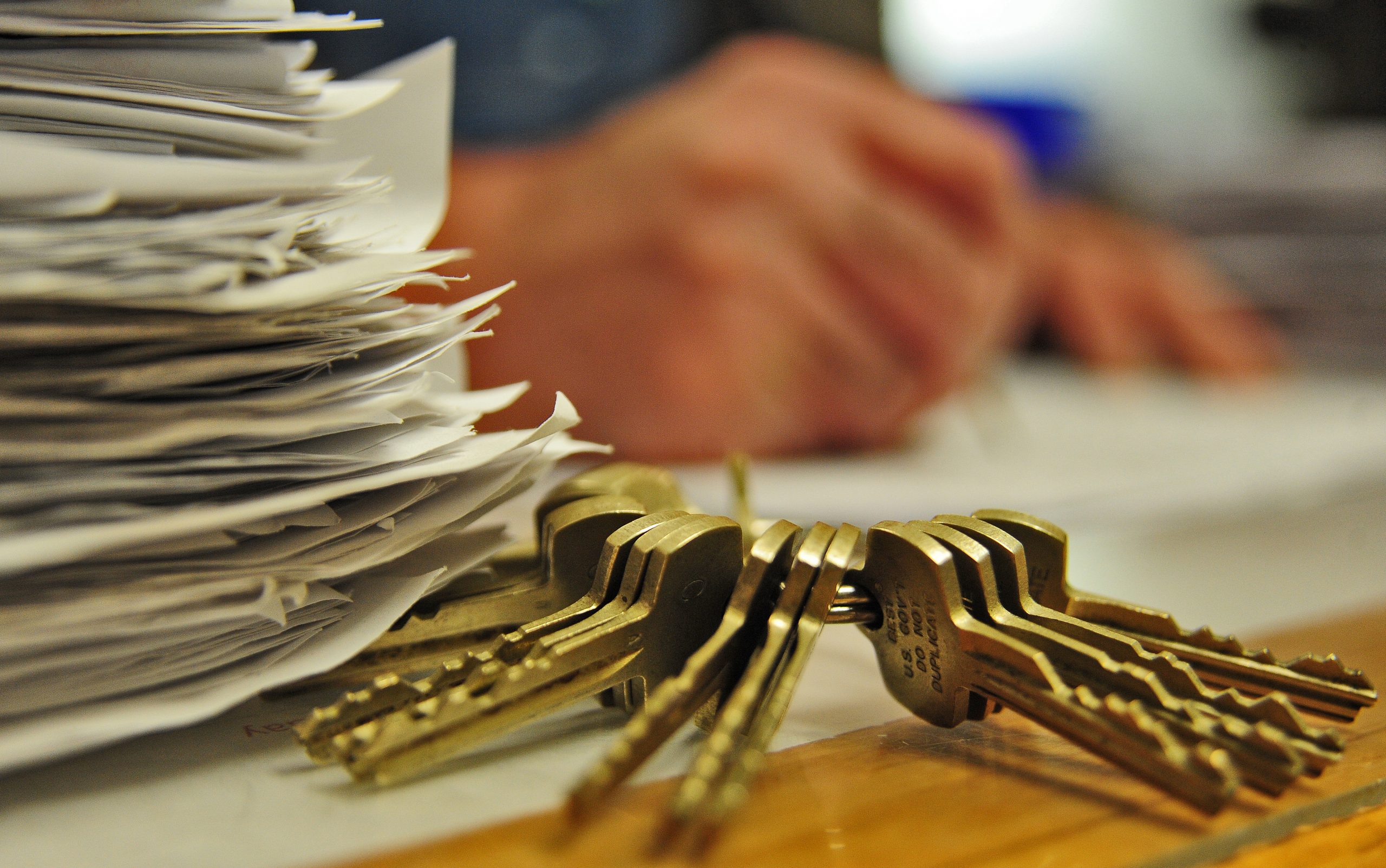 Stack of cut brass keys on a bench with a hand reaching past