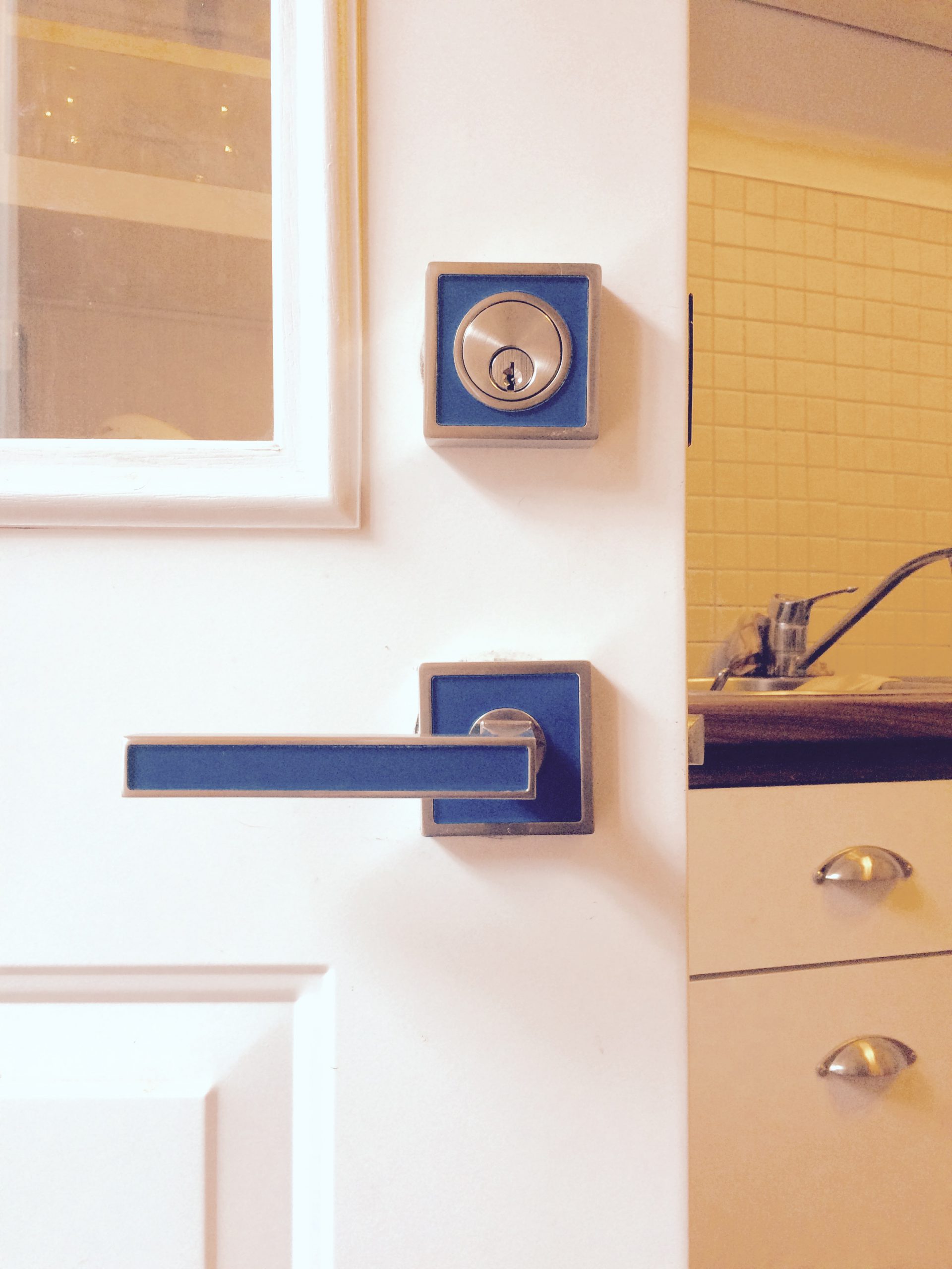 Blue deadbolt and matching lever on a white door beside a cabinet