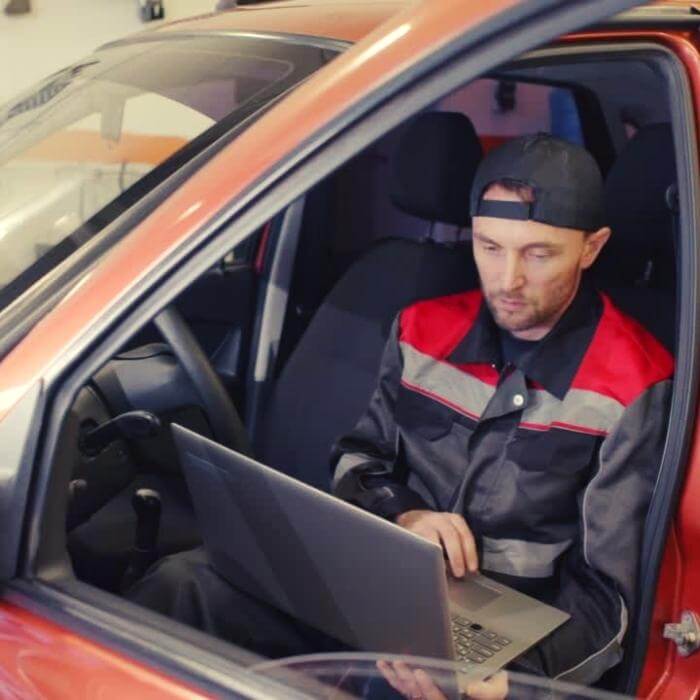 Technician working on a laptop in the driver seat of a red car