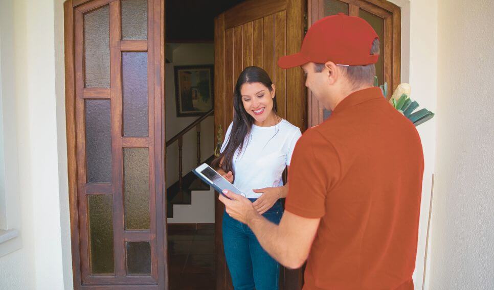 Delivery driver handing a package to a smiling woman at the front door