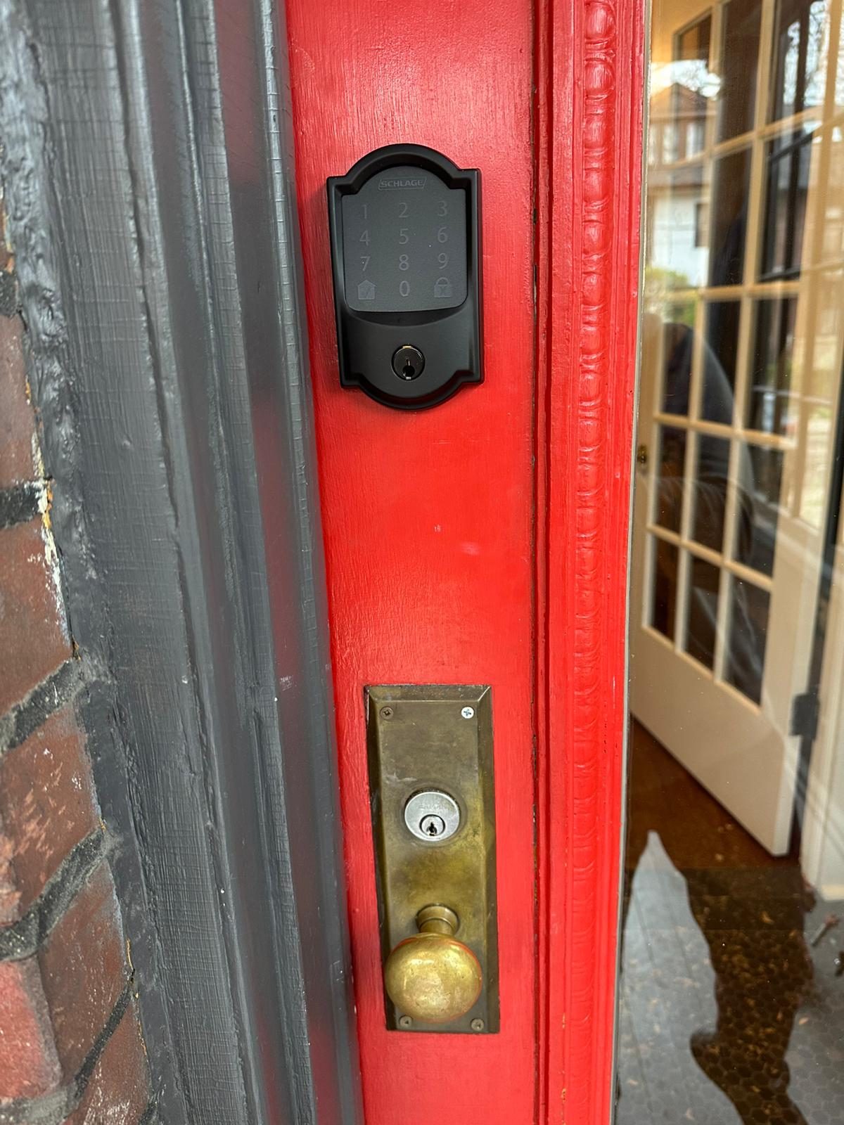 Black electronic lock fitted above brass hardware on a red door