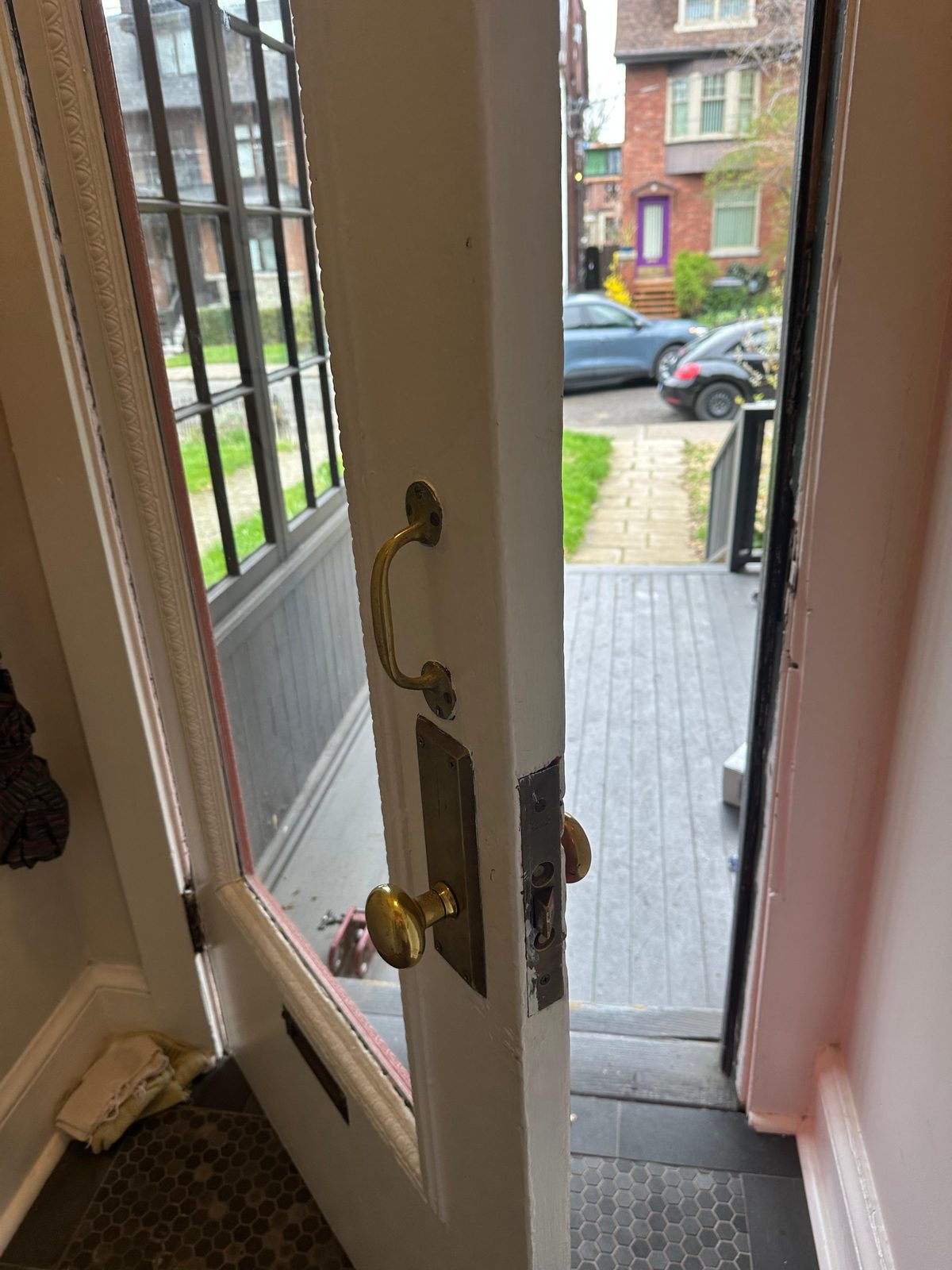 Open entrance door with a brass handleset, looking out to the street