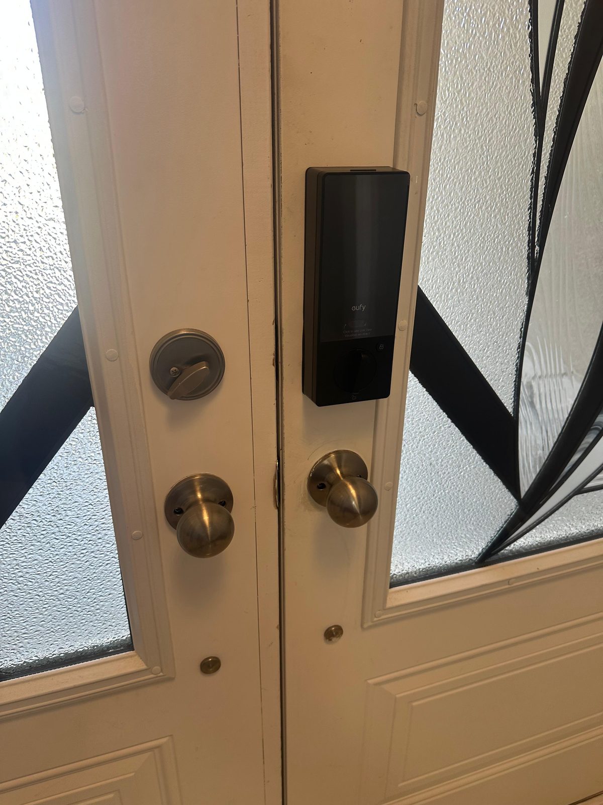 Black smart lock and brass knob on a white door with leaded glass panels