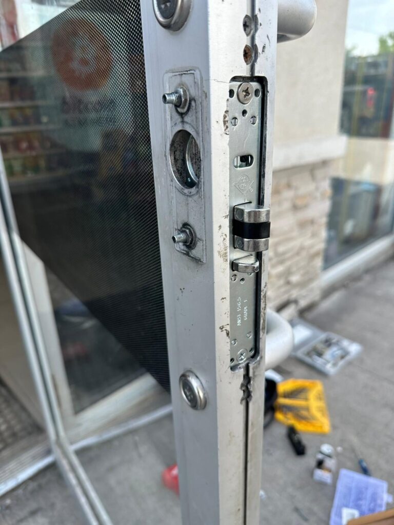 Storefront door hardware partly removed with tools on the mat below