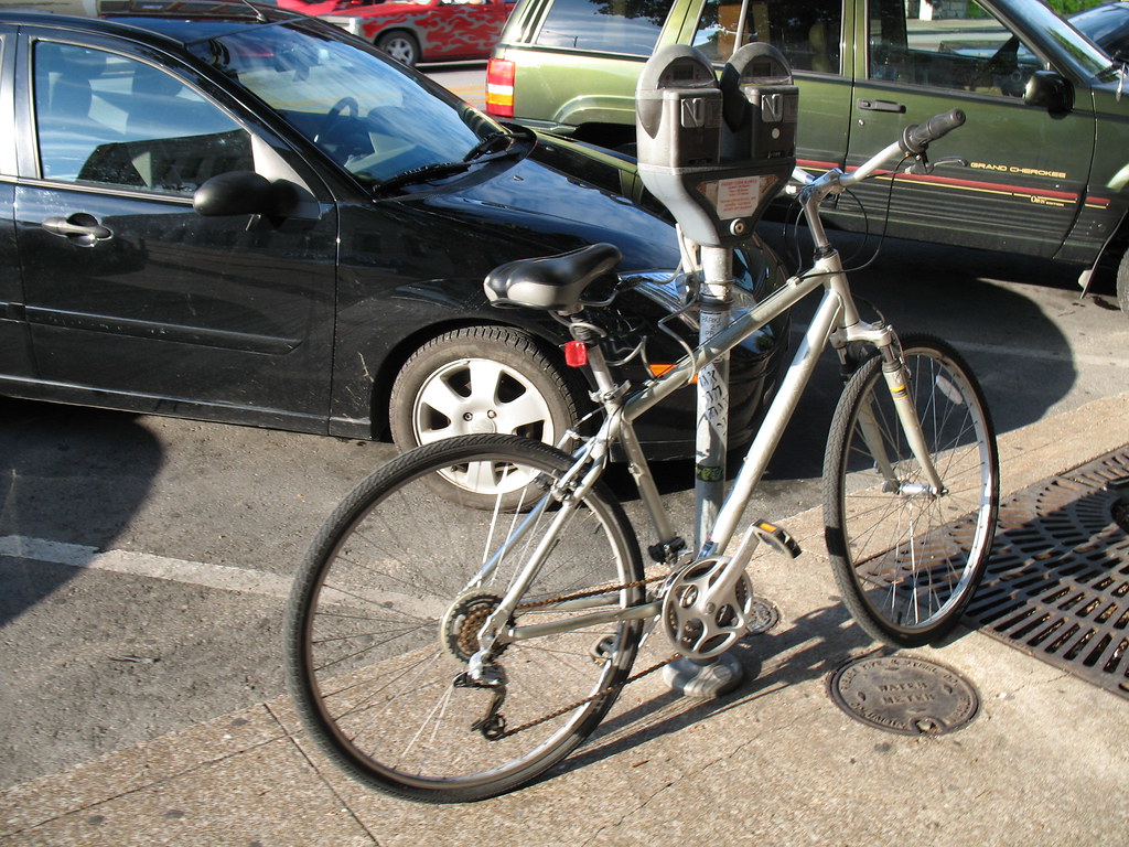 Bicycle locked to a post beside parked cars